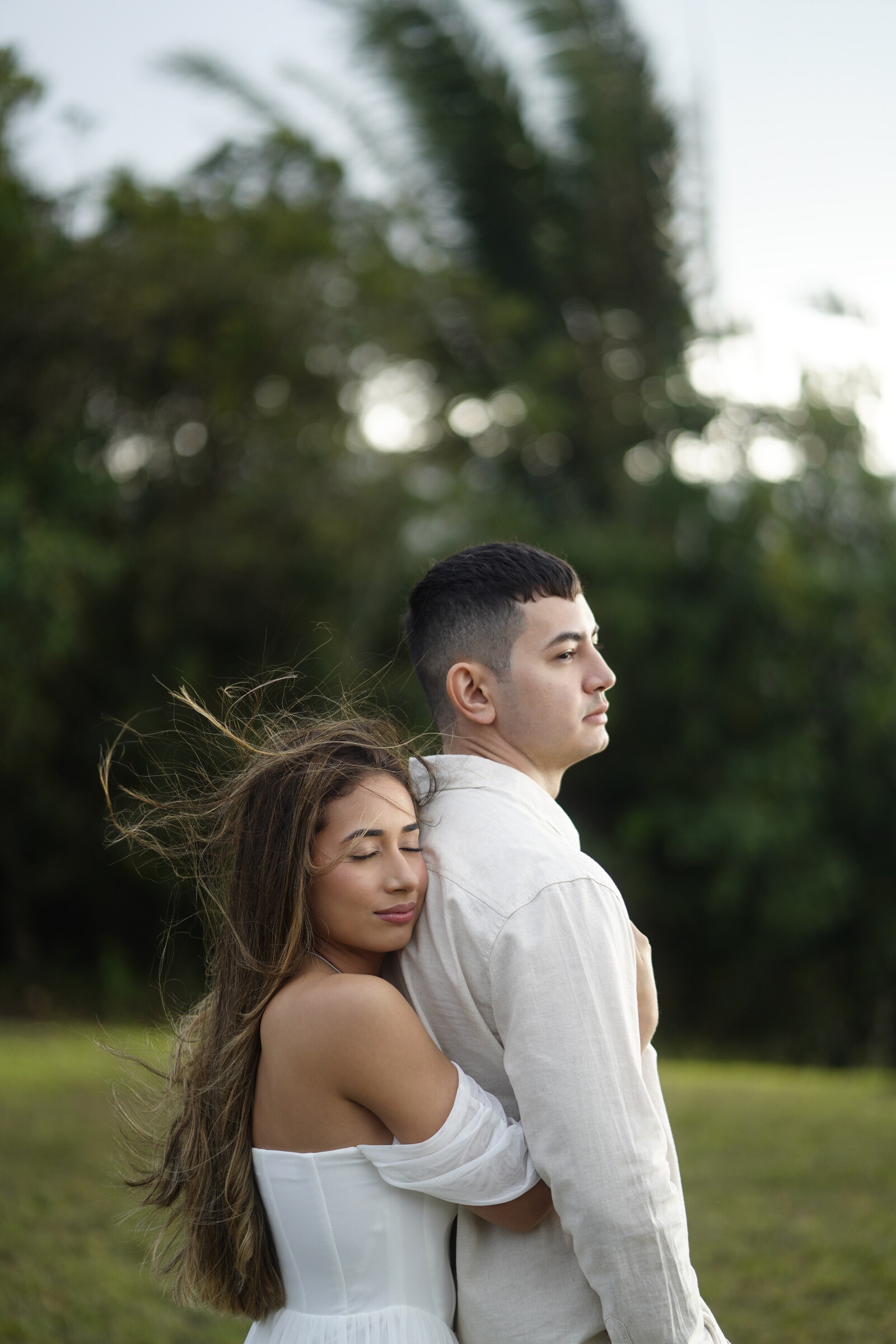 Danielle abraça Felipe por trás e apoia o rosto em suas costas, o cabelo ao vento